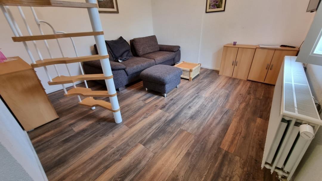 Living room with sofa, ottoman, and wooden floor. Stairs lead upstairs.