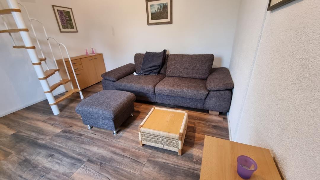 Living room with sofa, ottoman, and wooden floor. Pictures hang on the wall.