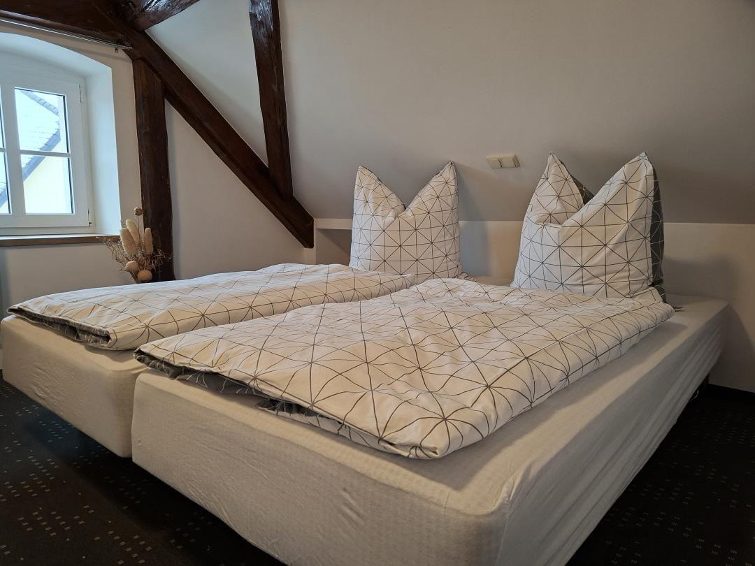 Zwei Betten mit gemusterten Bettwäsche unter Holzbalken in einem Schlafzimmer mit Fenster.