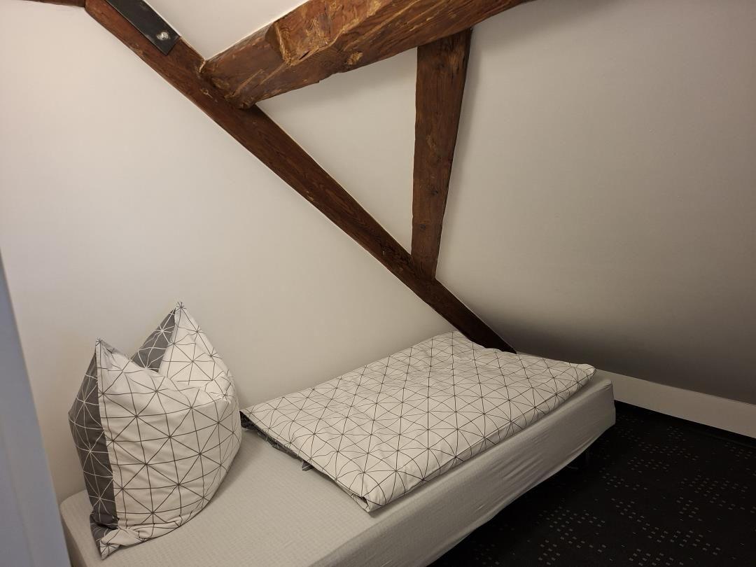 Ein Bett mit Kissen unter Holzbalken in einem Dachzimmer.