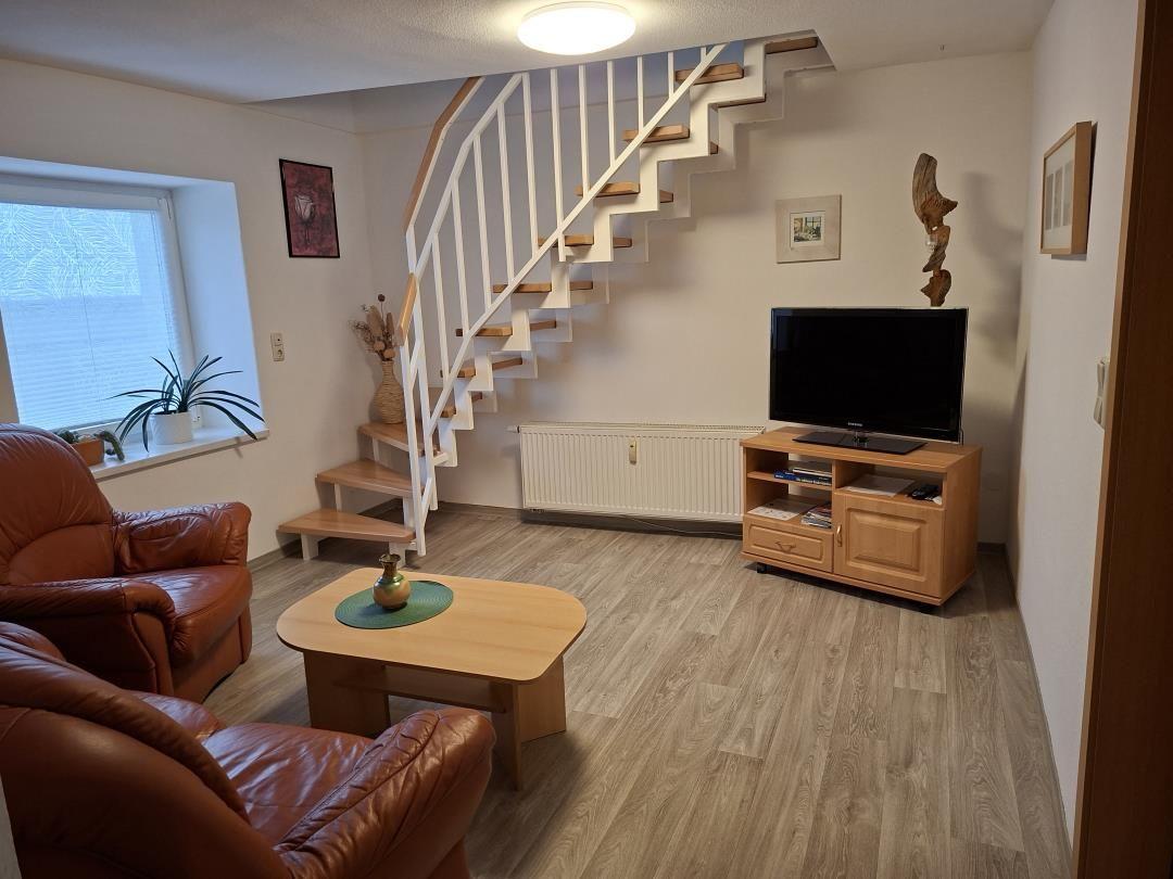 Wohnzimmer mit Holzboden, Sitzgelegenheit, Fernseher und Treppe.