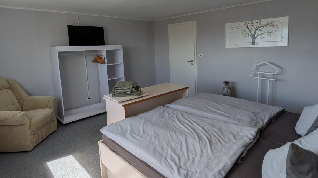 Schlafzimmer mit Doppelbett, Kleiderschrank, Sessel und Fernseher.