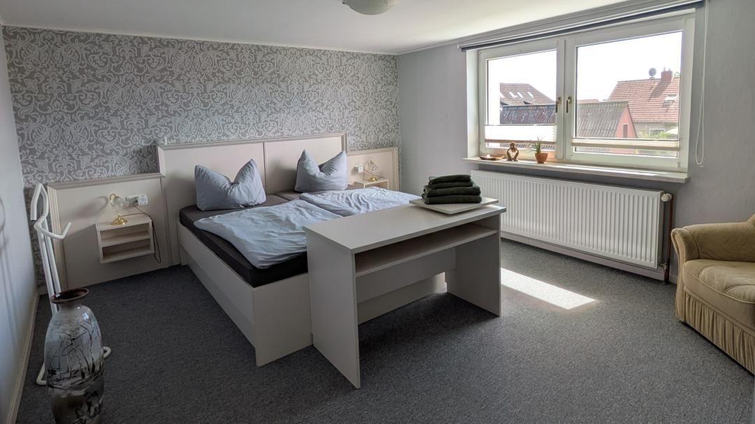 Schlafzimmer mit Bett, Schreibtisch und Fenster mit Blick auf Dächer.