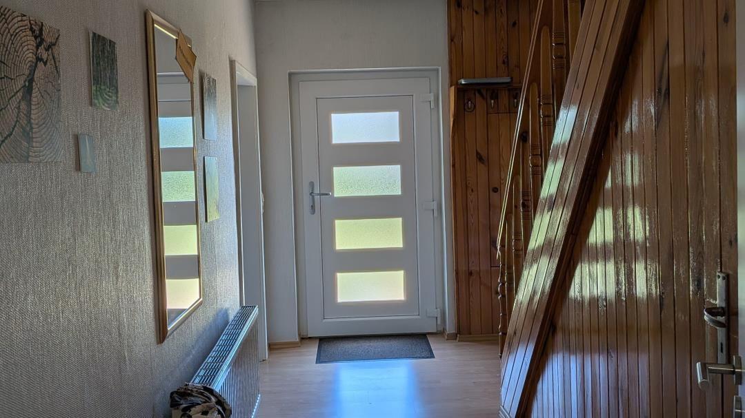 Hausflur mit Holztreppe, weiße Tür mit Glasfeldern und Wandbildern.