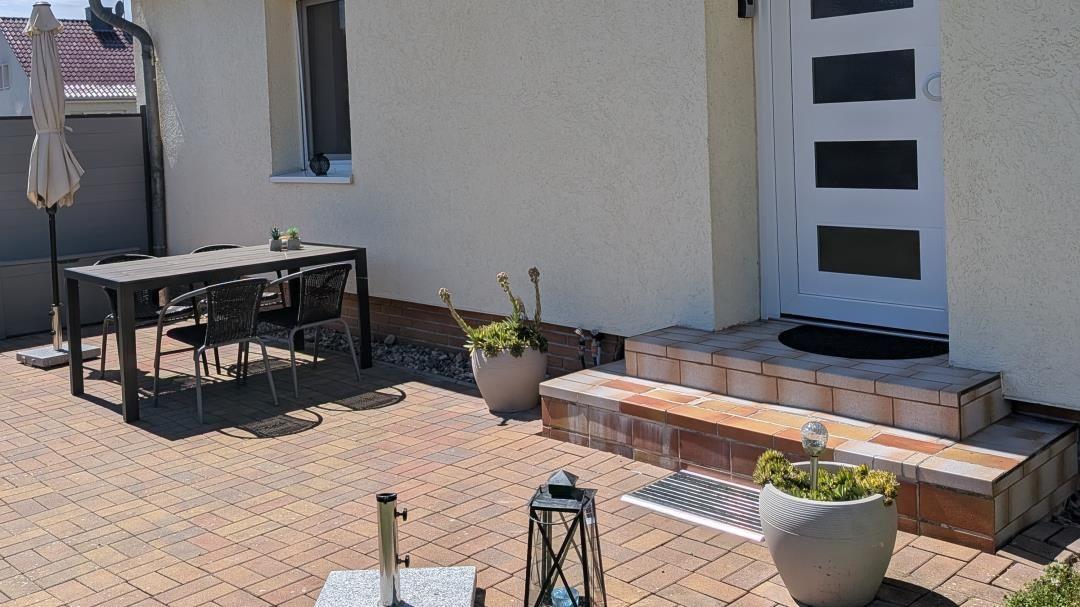 Terrasse mit Tisch, Stühlen und Pflanzen vor Haus mit weißen Türen.