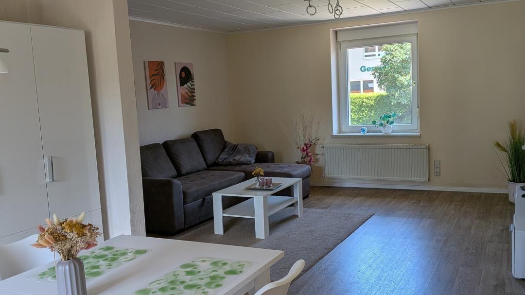 Wohnzimmer mit Sofa, Tisch und Fenster. Holzboden und Wandbilder.