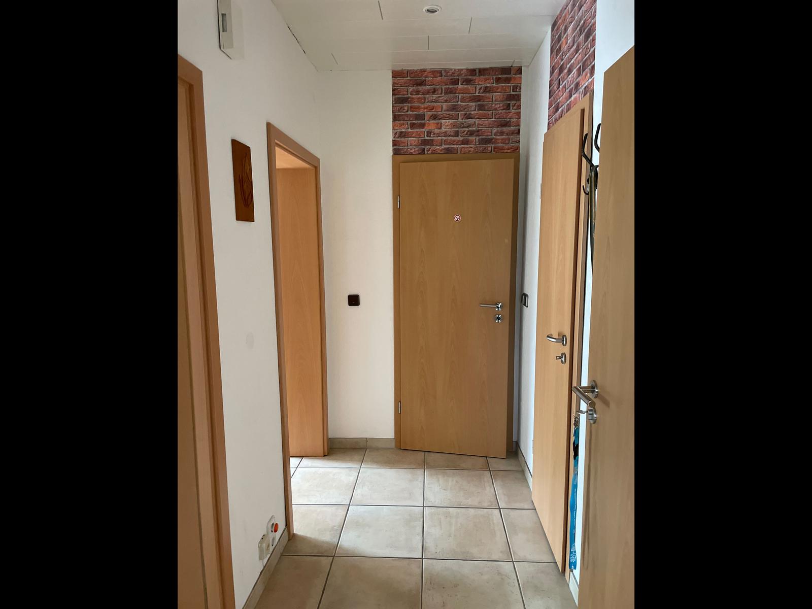 Hallway with wooden doors and tiled floor. Brickwork is on one wall.