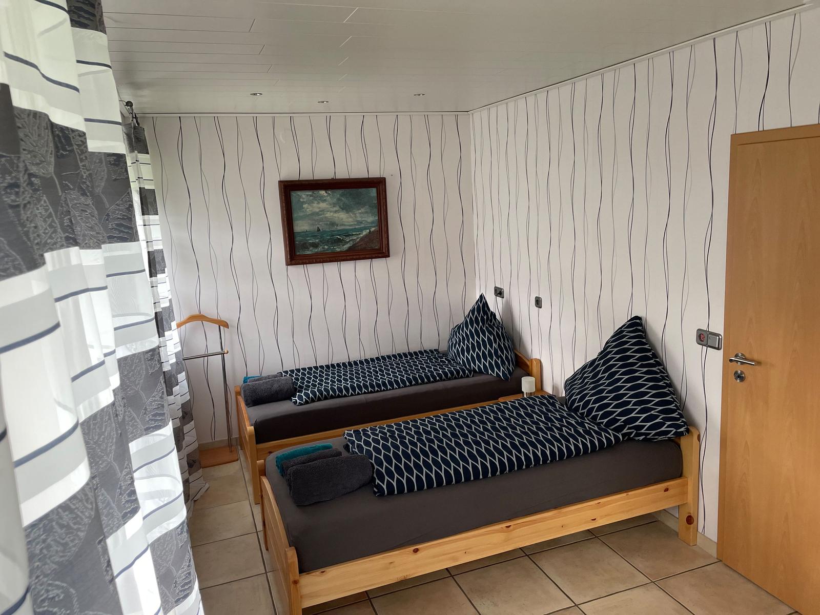 Two single beds with dark blue bedding and pillows. Wall with stripes, picture, and door.
