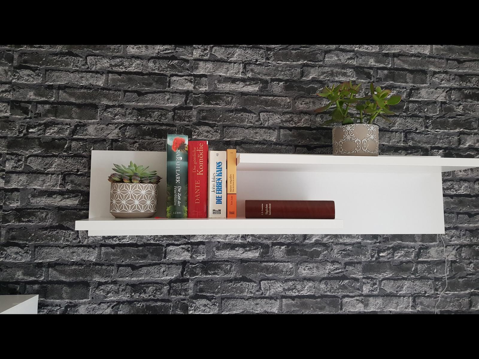 White shelves with books and plants against a brick wall.