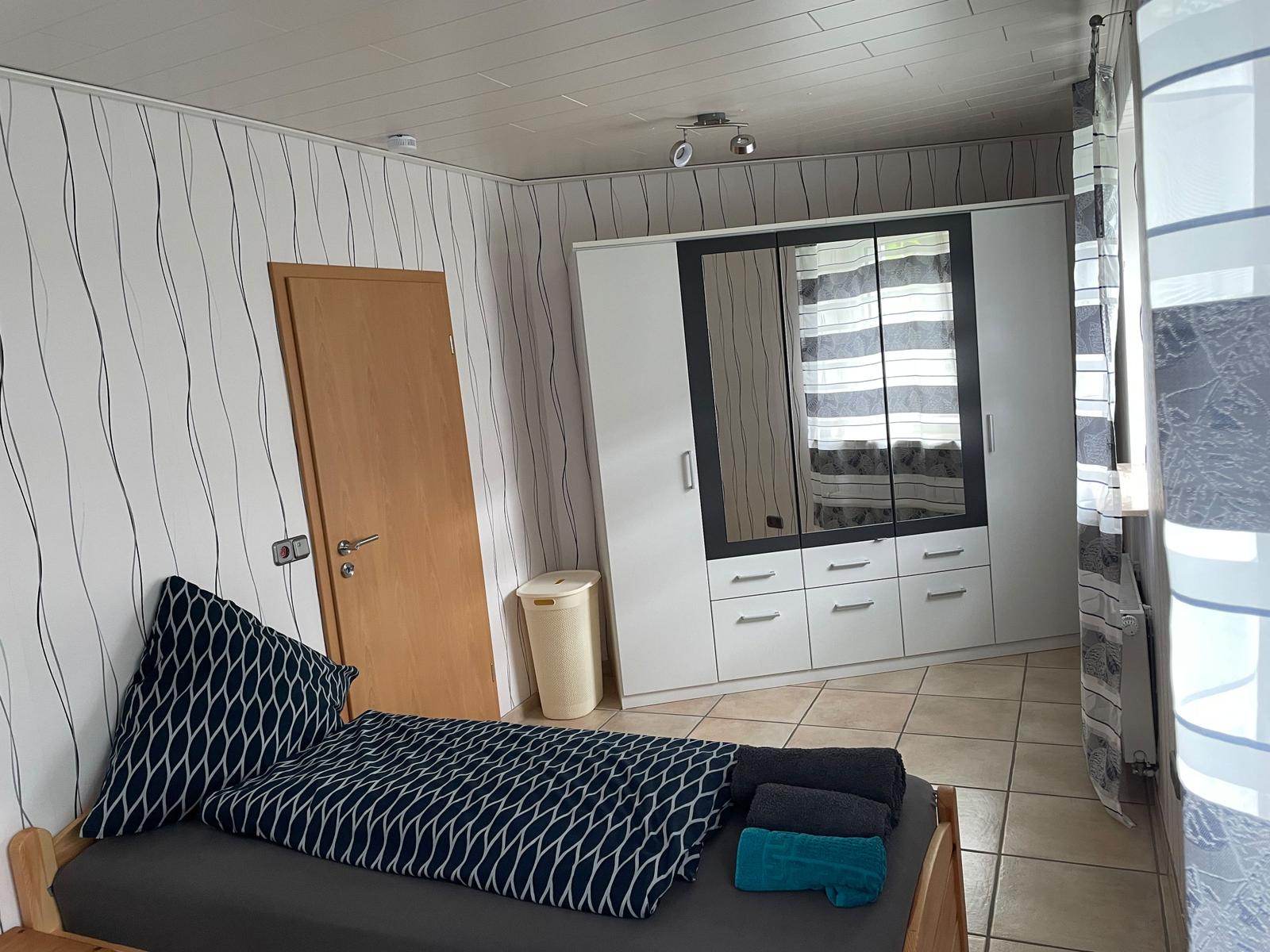 Bedroom with bed, wardrobe, and window. Walls with striped wallpaper.