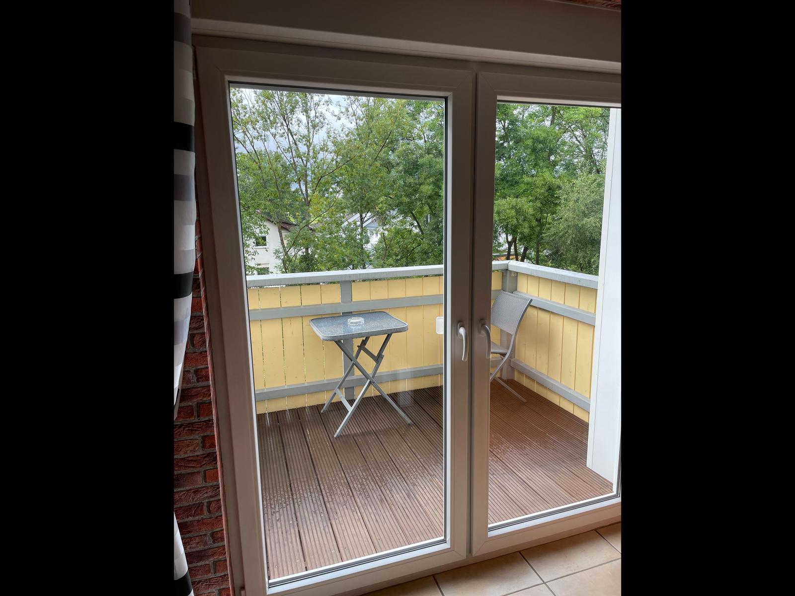 Balcony with table and chair, yellow wood paneling and view of trees.
