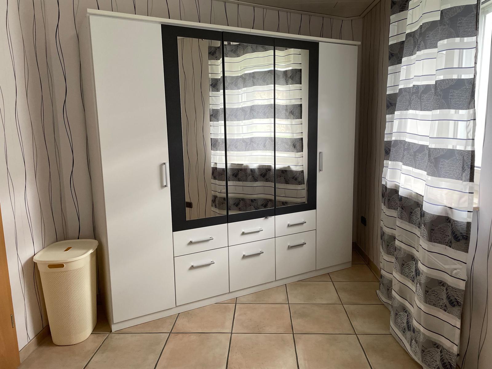 Bedroom with white wardrobes, mirrored doors, and window with curtains.