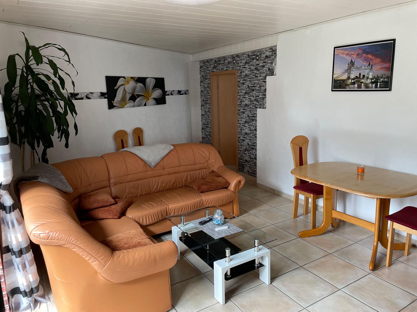 Living and dining area with brown sofa, glass table, and wooden table with chairs.