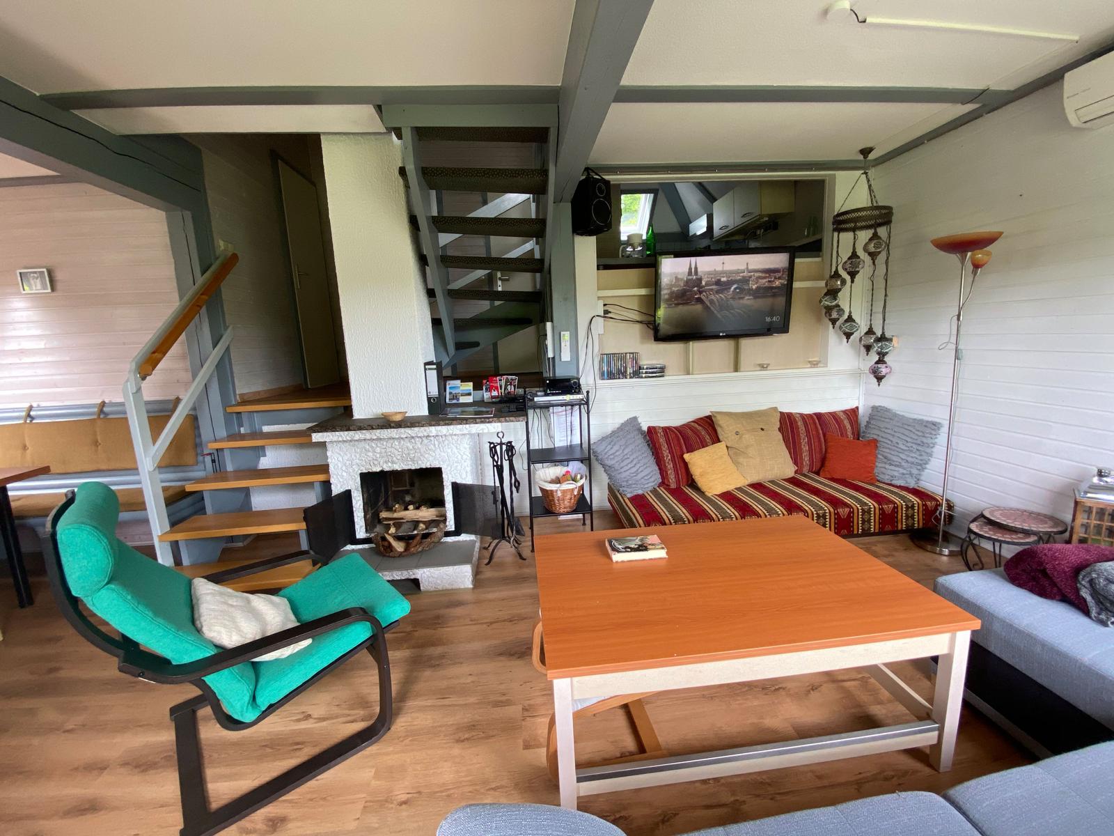 Wohnzimmer mit Kamin, Sofa und Fernseher. Treppe führt zur oberen Etage.