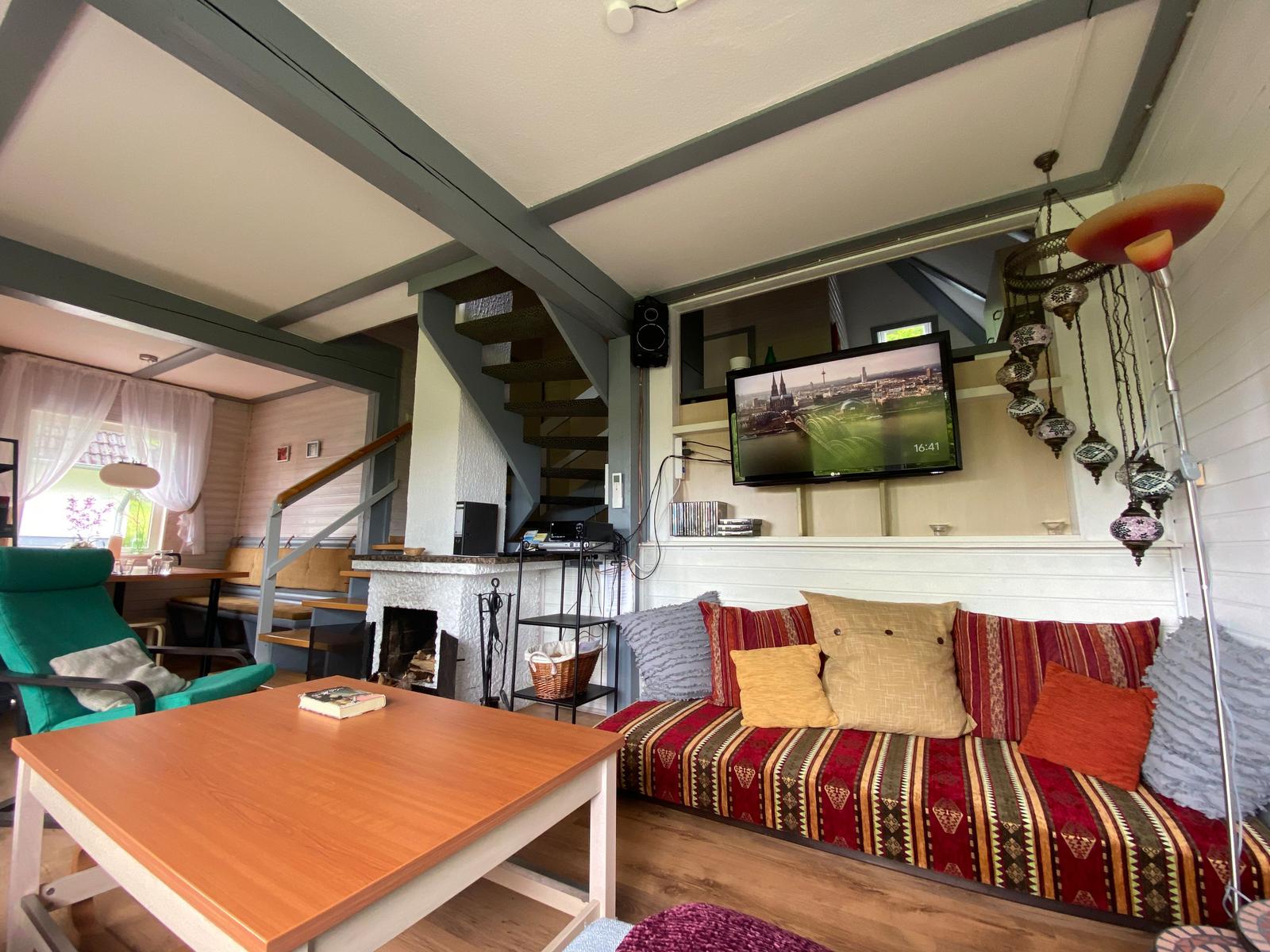 Wohnzimmer mit Sofa, Fernseher und Kamin. Treppe führt nach oben.
