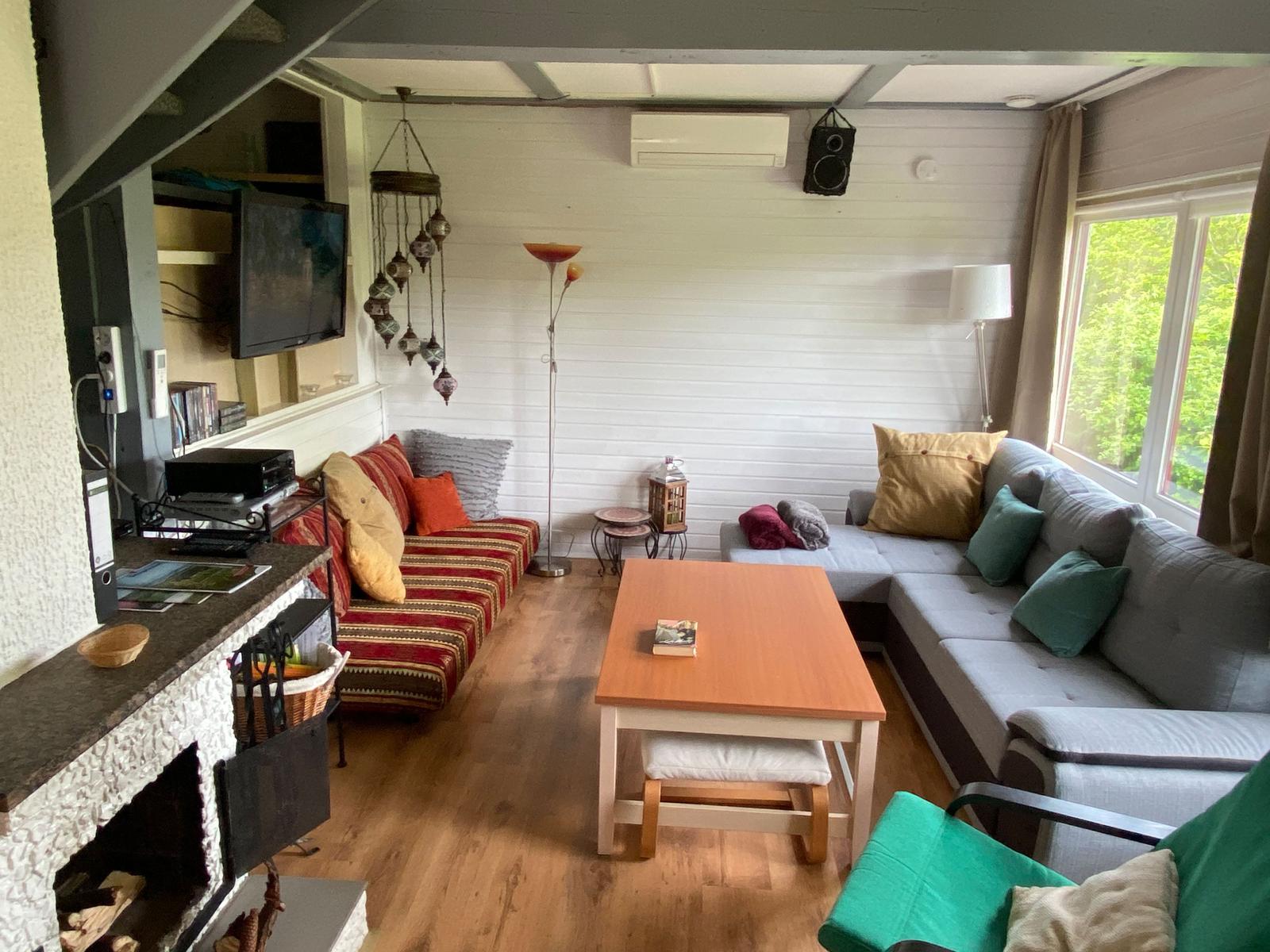 Wohnzimmer mit Sofa, Couchtisch und Kamin. Fenster mit Blick auf Grün.