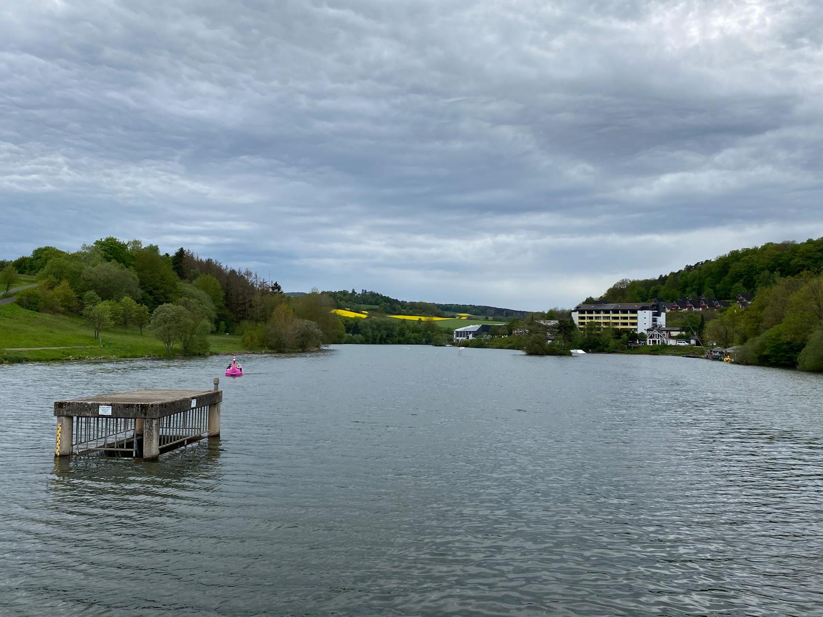 See mit Steg, Boot und Hotel im Hintergrund unter bewölktem Himmel