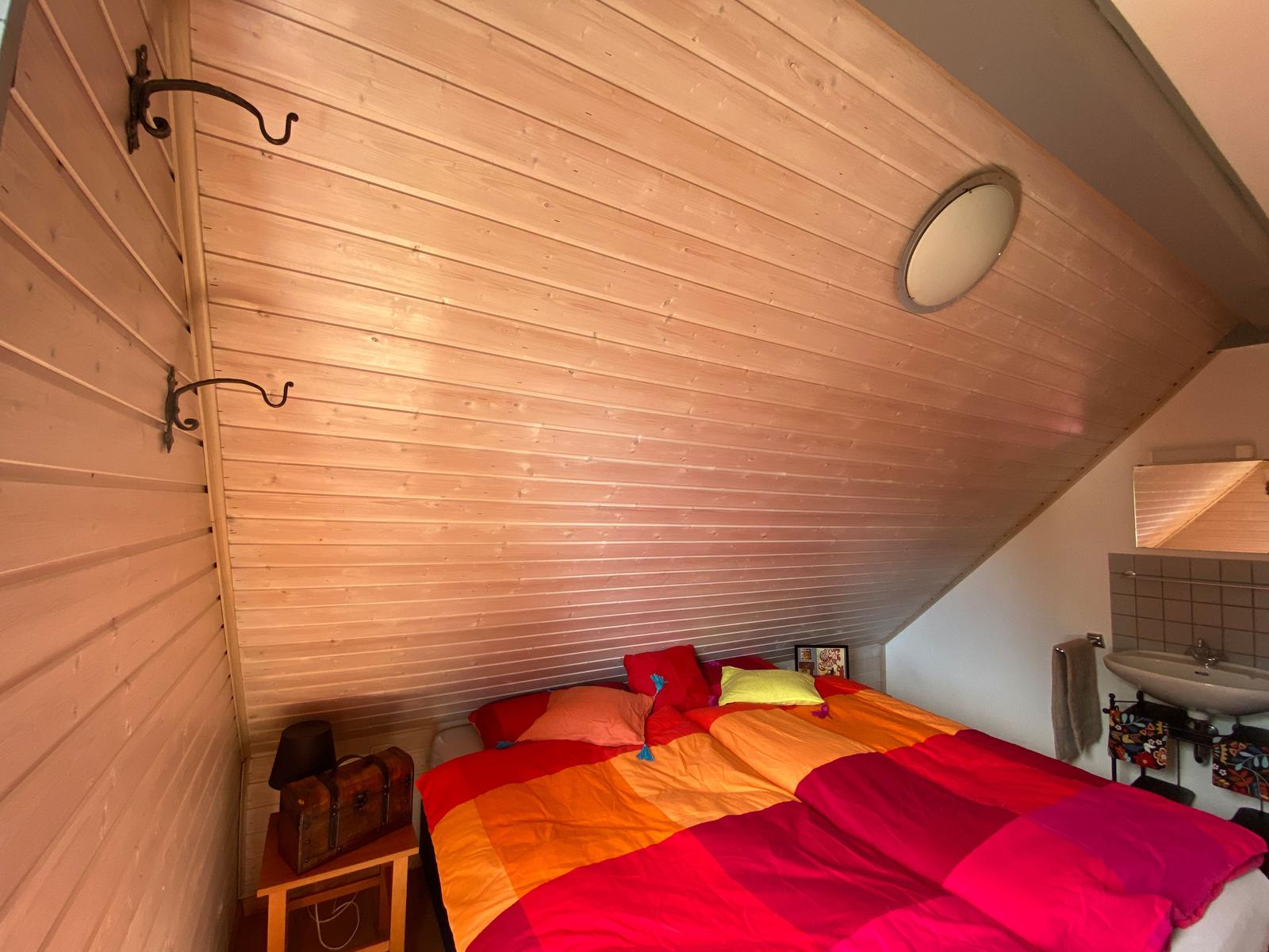 Schlafzimmer mit Holzwand, Bett mit buntem Bettzeug und Waschbecken.