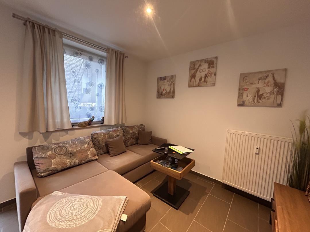 Wohnzimmer mit Sofa, Tisch und Fenster. An den Wänden hängen Bilder.