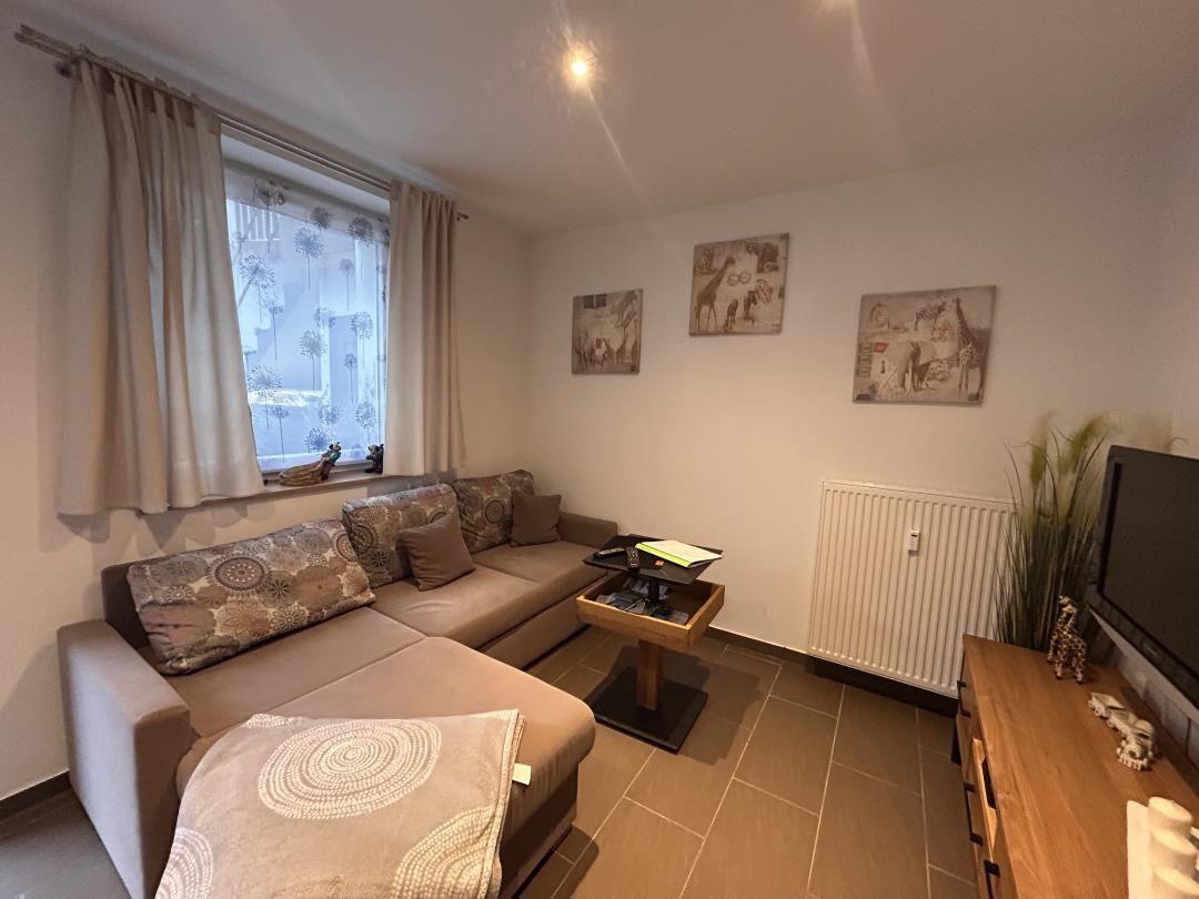 Wohnzimmer mit Sofa, Couchtisch und Fernseher. Fenster mit Vorhängen und Wandbilder.