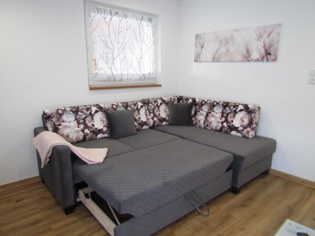 Ein Ecksofa mit floralen Rückenkissen und einem ausziehbaren Bettteil.