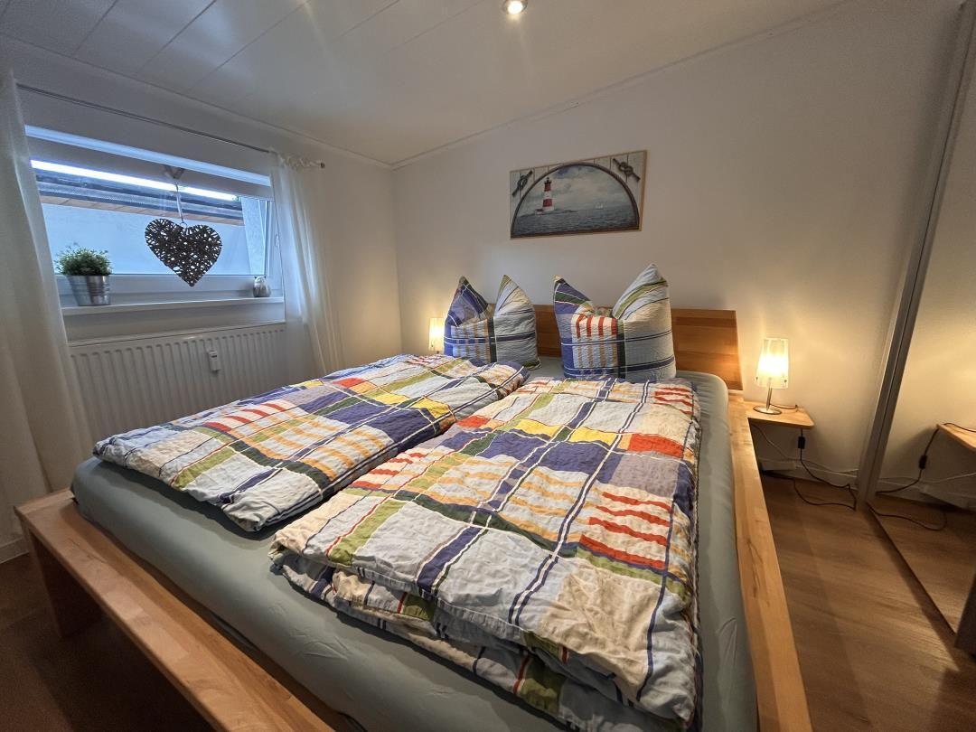 Schlafzimmer mit Doppelbett, Holzrahmen, Fenster und Wandbild mit Leuchtturm.