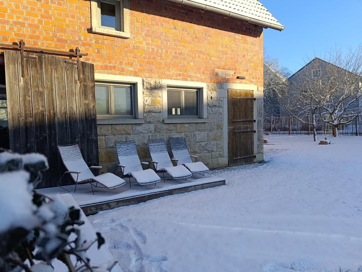 Schneebedeckte Liegestühle vor einer Backsteinmauer mit Holztür und Fenstern.