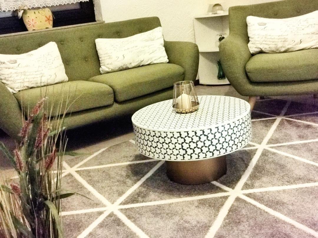 Ein Wohnzimmer mit grünen Sofas, einem runden Tisch und einem gemusterten Teppich.
