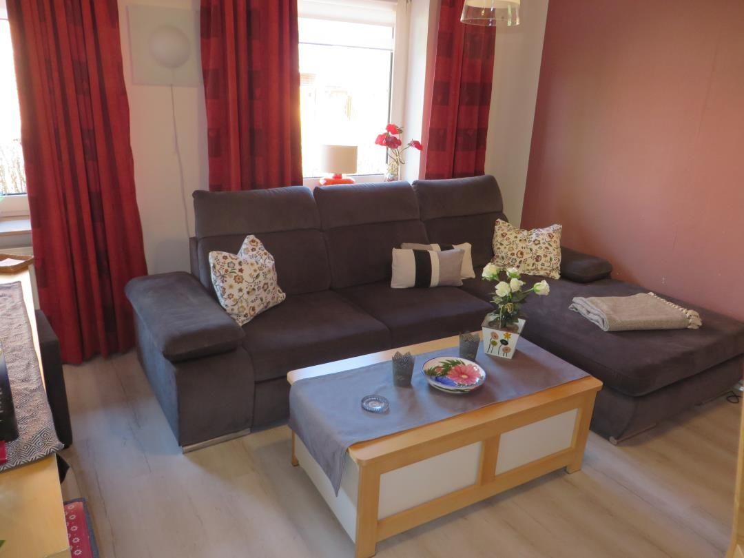 Ein Wohnzimmer mit braunem Sofa, Holzcoffee-Tisch und roten Vorhängen.