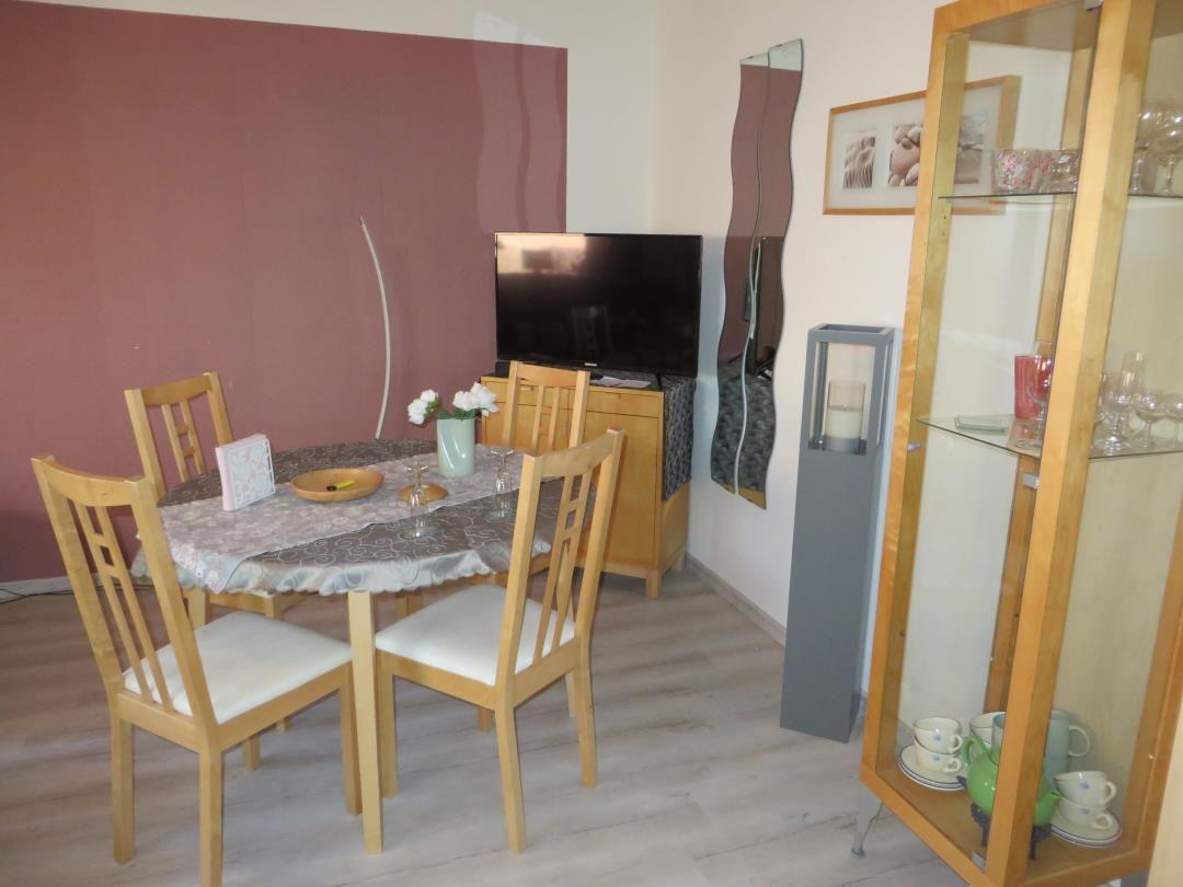 Esszimmer mit Tisch, Stühlen, Fernseher und Glasvitrine.
