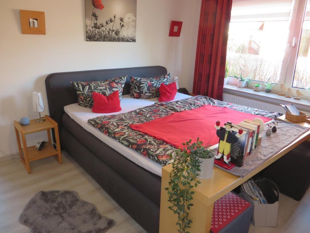 Schlafzimmer mit Bett, Nachttisch und Fenster mit roten Vorhängen.
