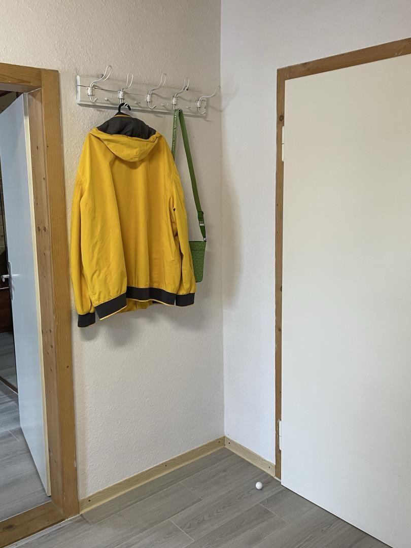 Ein gelber Jacke und eine grüne Tasche hängen an einem Haken an der Wand.