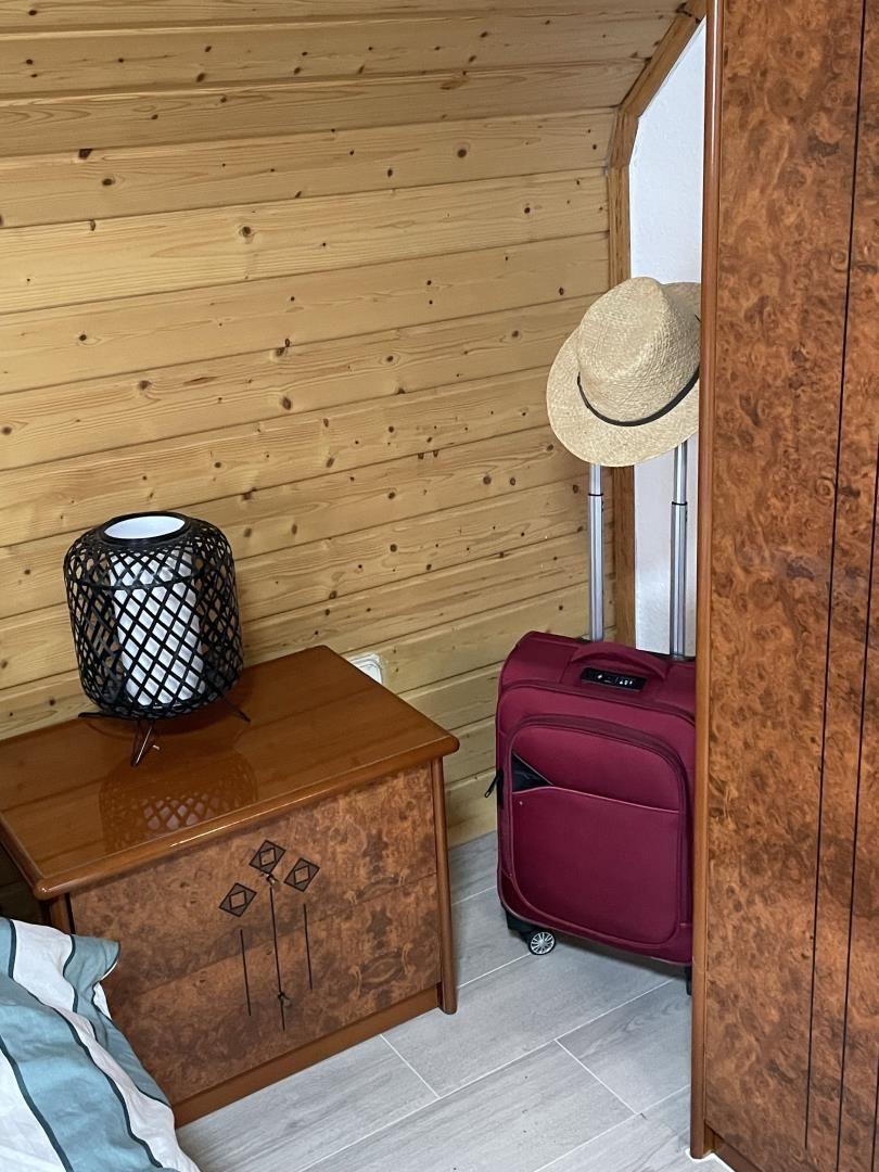 Schlafzimmer mit Holzwand, Nachttisch, Lampe und rotem Koffer.