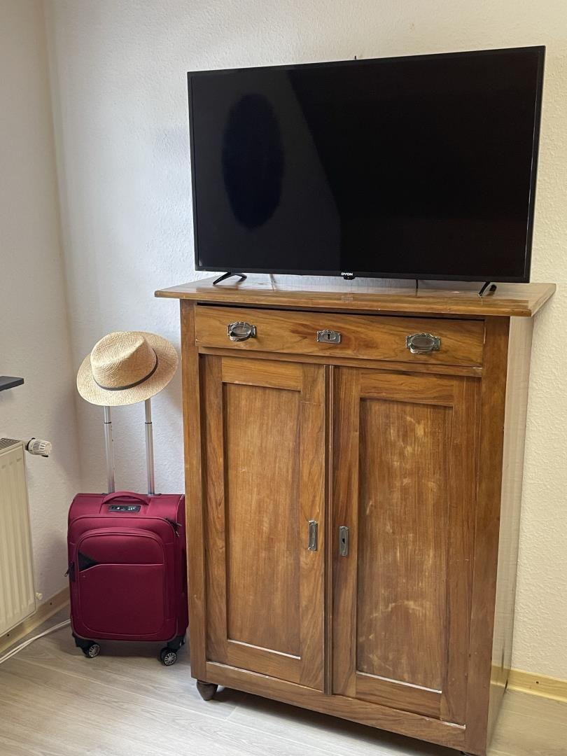 Holzschrank mit Fernseher und roter Reisetasche mit Strohhut