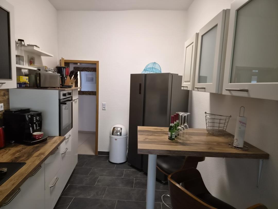 Küche mit Kühl-Gefrierkombination, Esstisch und Arbeitsplatte aus Holz.