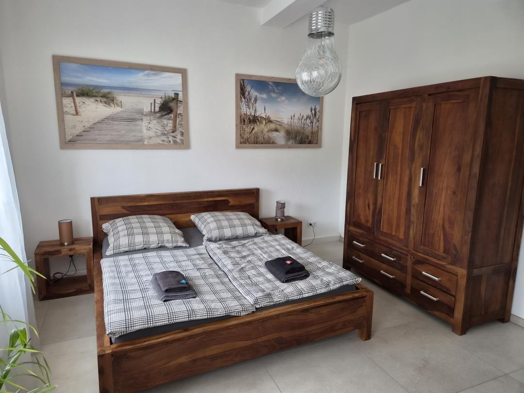 Schlafzimmer mit Holzbett, Kleiderschrank und Strandbildern an der Wand.