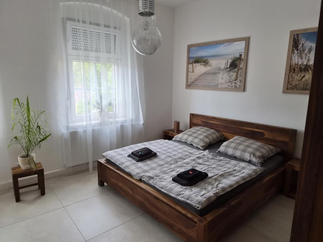 Schlafzimmer mit Holzbett, Fenster mit Vorhängen und Wandbildern.