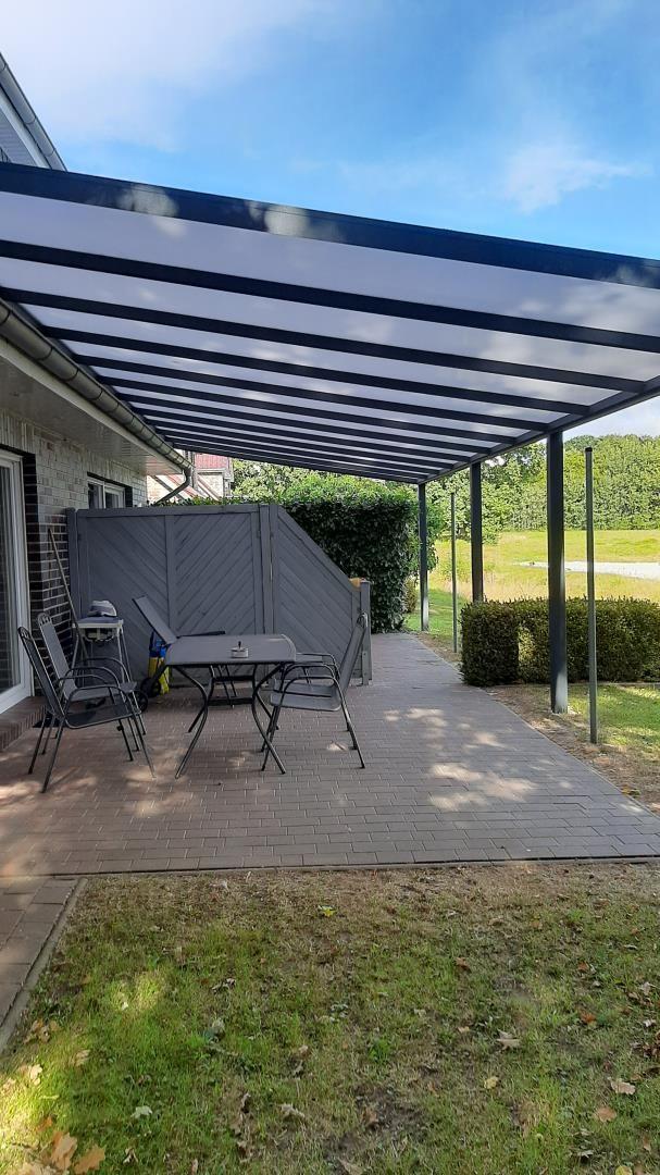 Terrasse mit Tisch und Stühlen unter einem schwarz-weißen Markisen-Dach.
