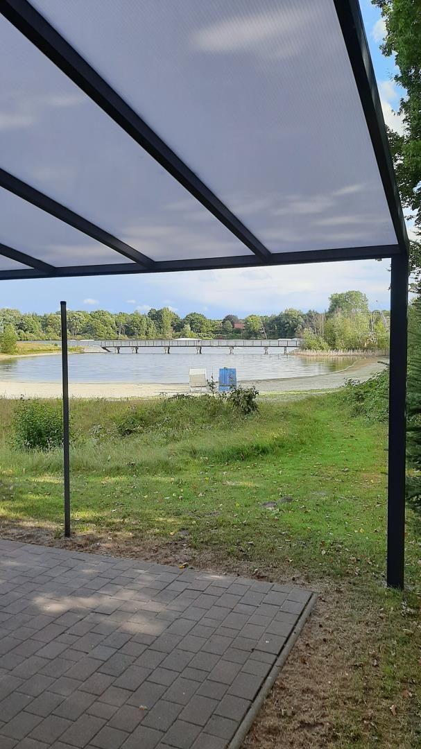 Sicht unter einer Markise auf einen See mit Strand und Steg.