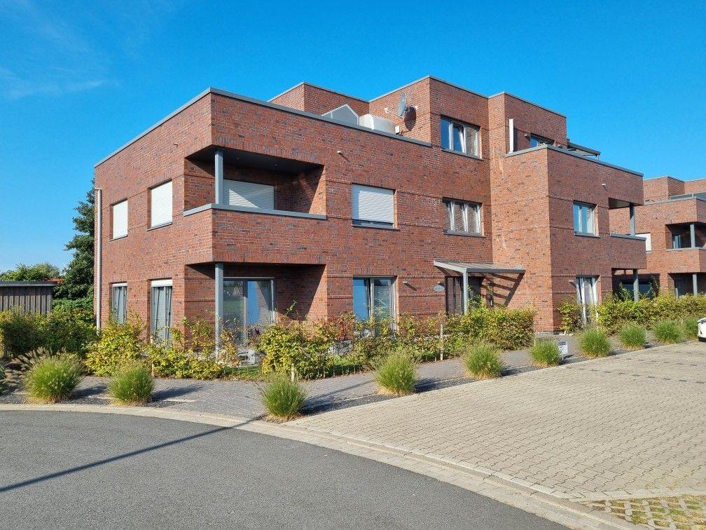 Moderne Wohnanlage aus rotem Backstein mit Balkonen und begrüntem Vorgarten.
