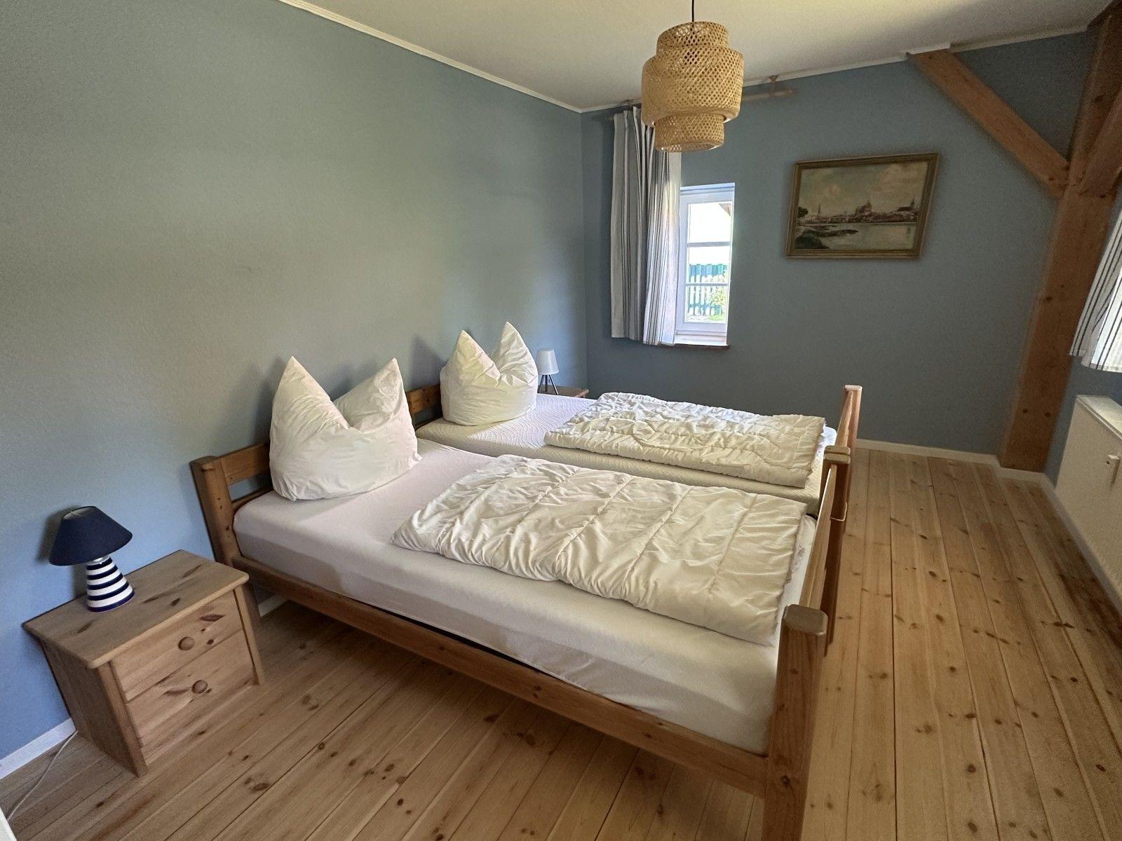 Schlafzimmer mit Doppelbett, Holzboden und Fenster. Holzrahmen an der Decke.