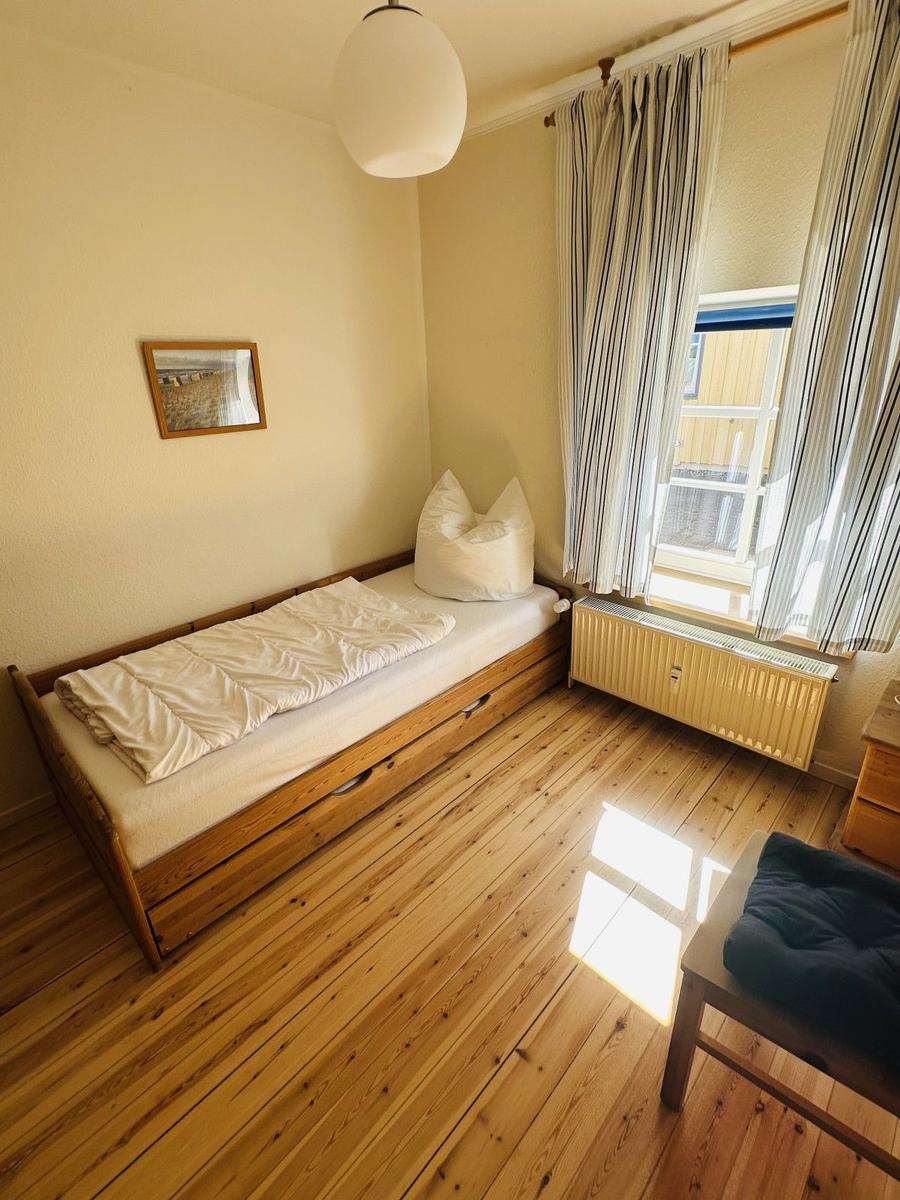 Ein Schlafzimmer mit Holzboden, einem Bett, einem Fenster und einem Stuhl.