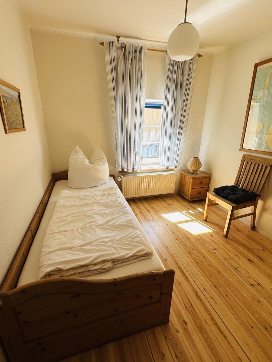 Ein Schlafzimmer mit Holzbett, Fenster mit Vorhängen und Holzfußboden.