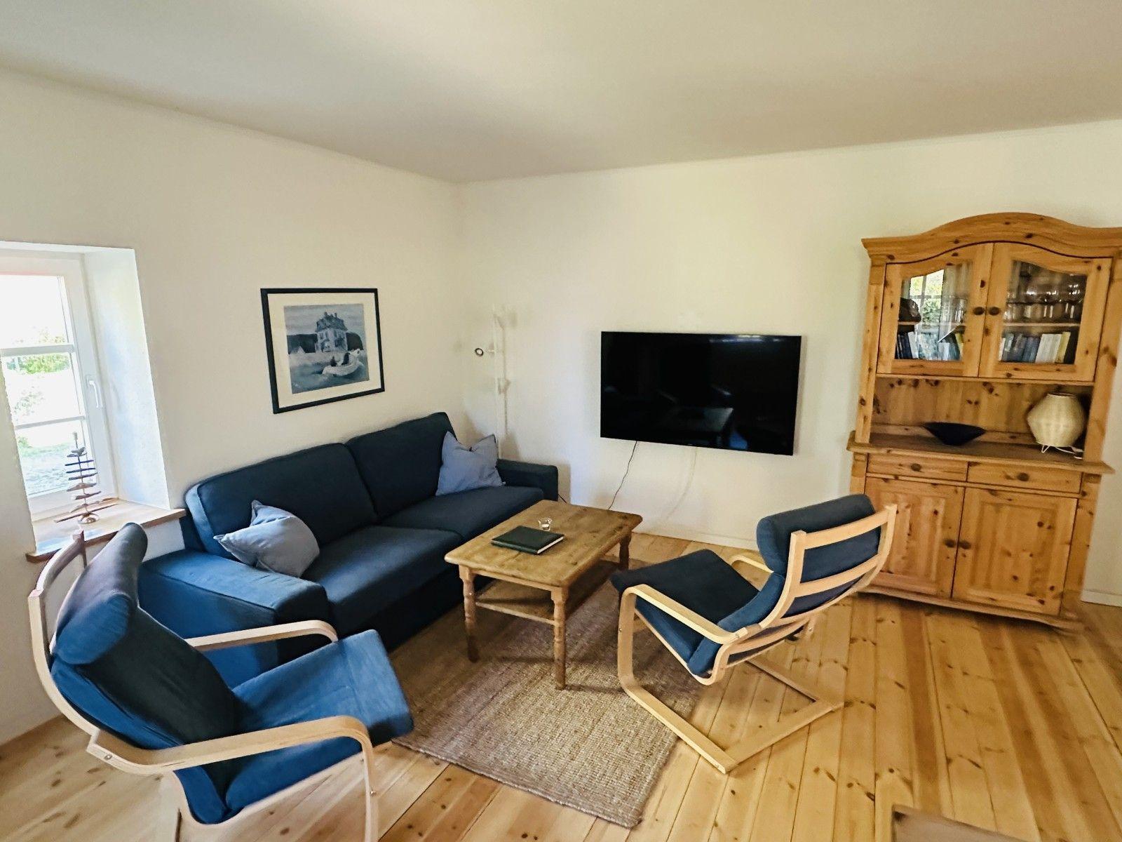 Wohnzimmer mit Sofa, zwei Stühlen, TV und Holzschrank.