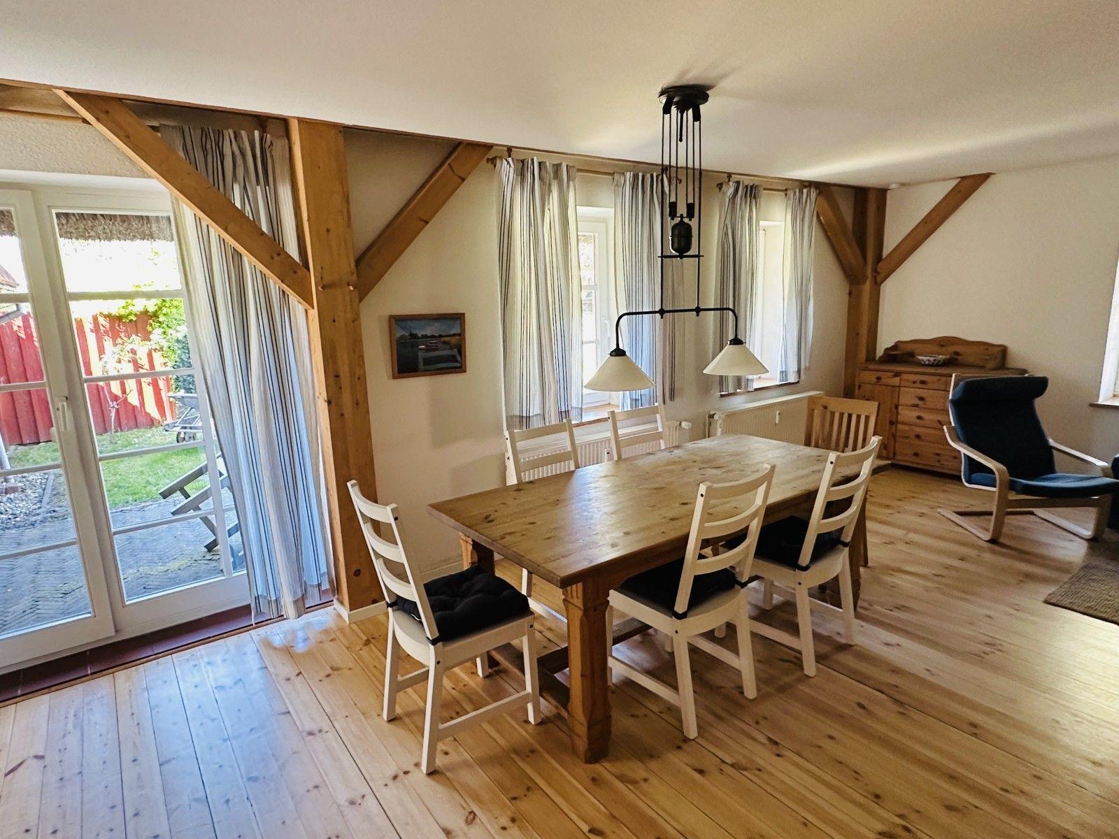 Esszimmer mit Holztisch, Stühlen und Fenstern. Holzdielenboden und Balken sichtbar.