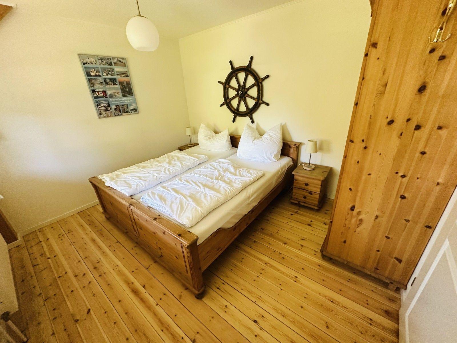 Schlafzimmer mit Holzbett, Navigationsrad an der Wand und Holzfußboden.