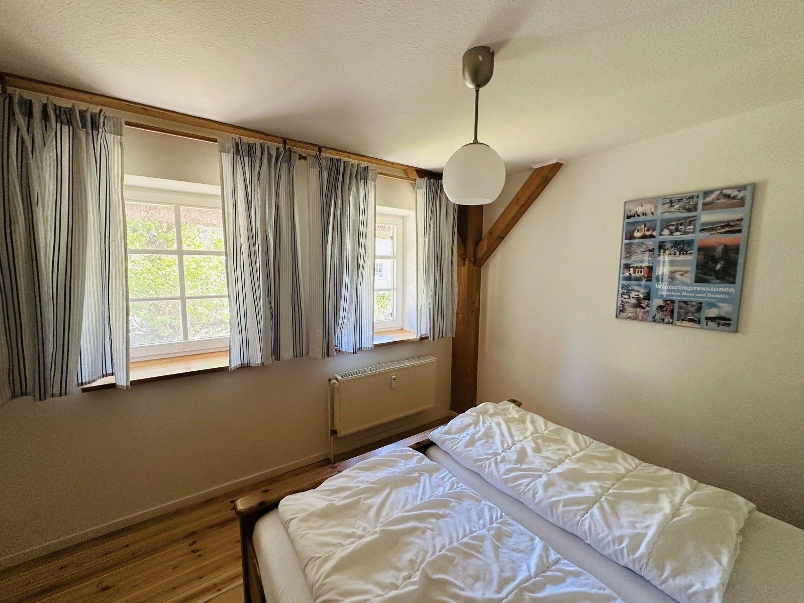 Ein Schlafzimmer mit Bett, Fenstern und Holzbalken.