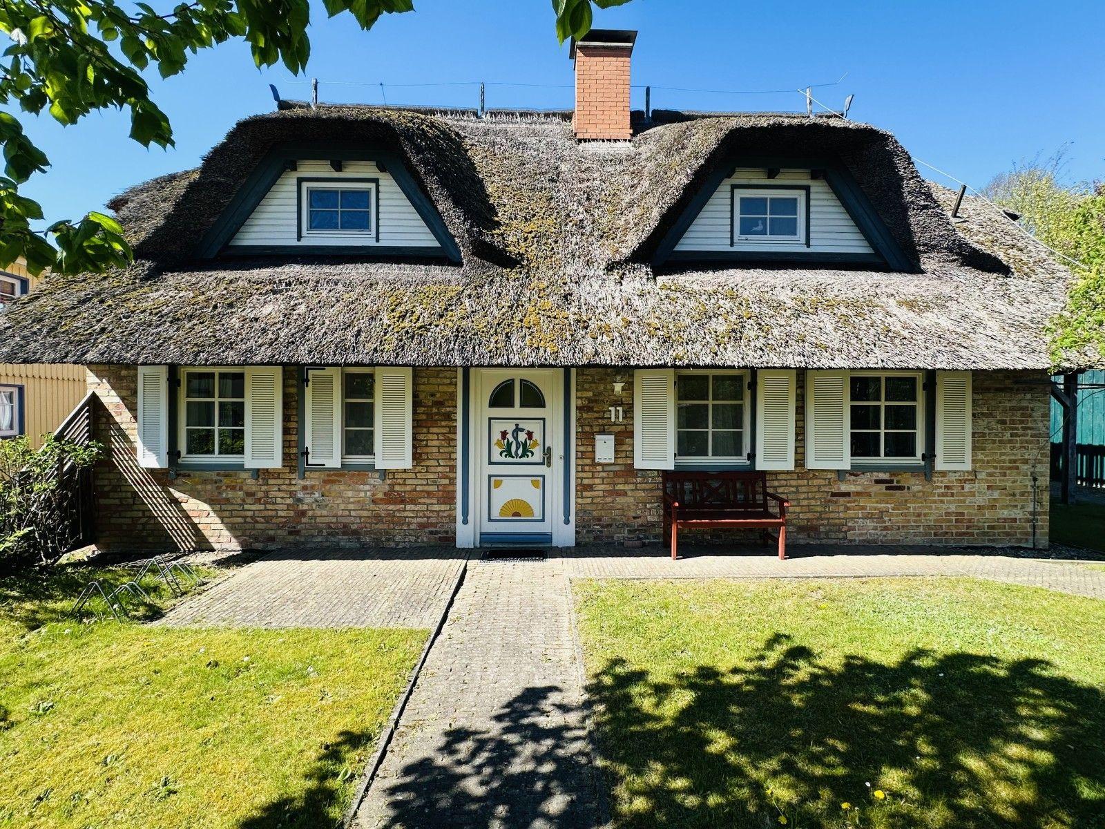 Haus mit Strohdach, weißer Tür und Fenstern mit weißen Läden.