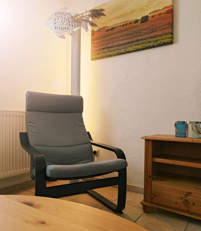 Ein grauer Sessel steht neben einem Holzregal und einer Wanddekoration.