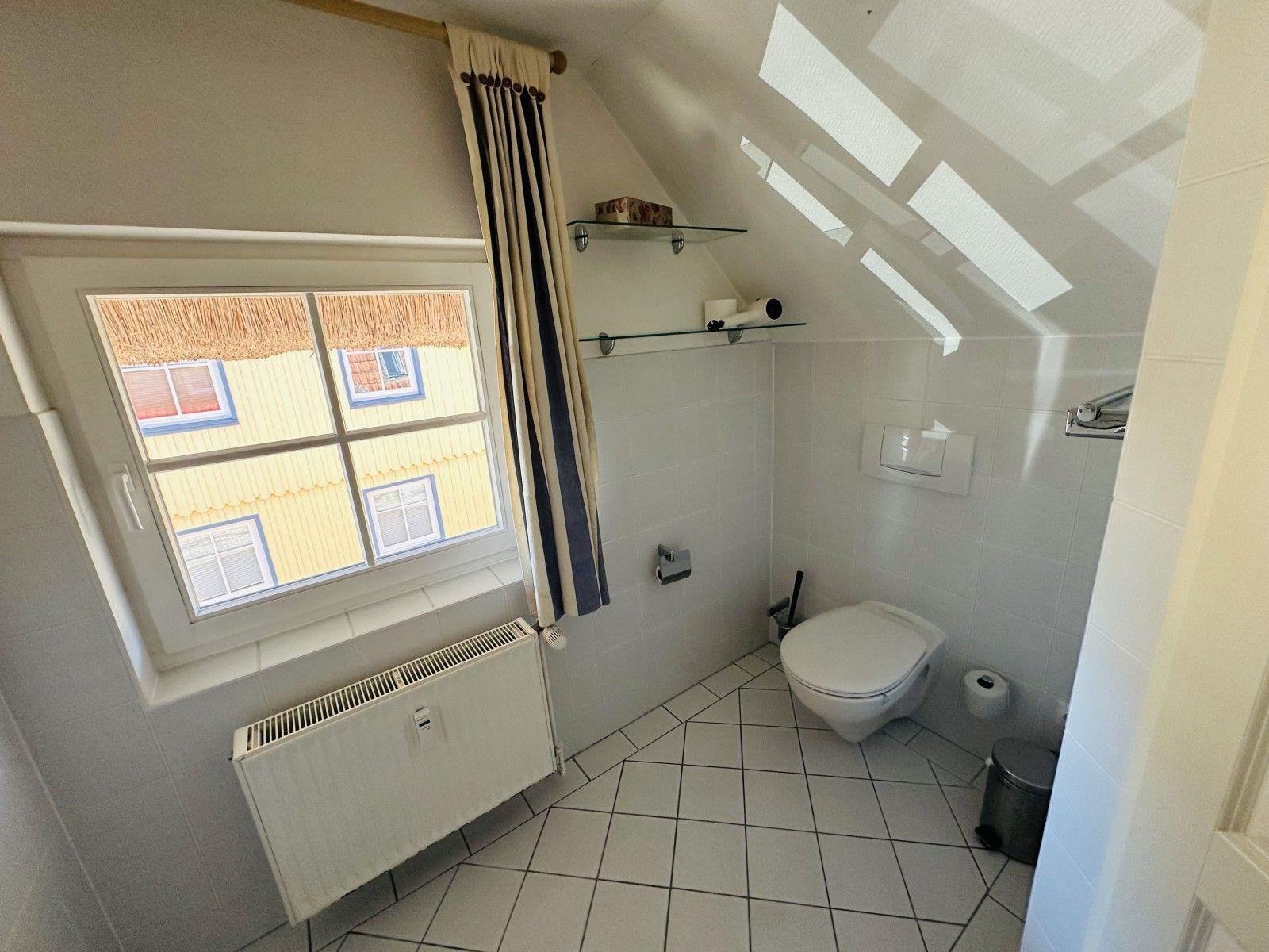 Badezimmer mit Toilette, Fenster und Dachschräge mit Dachfenstern.